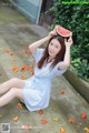 A woman sitting on the ground holding a slice of watermelon.